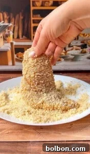 Mama's Italian Chicken Cutlets 10 A hand dips a cone-shaped pastry into a plate of breadcrumbs, with a bakery display of bread and pastries in the background.