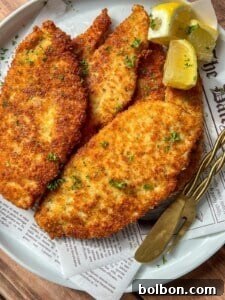 Mama's Italian Chicken Cutlets 13 A plate of golden, crispy breaded schnitzels garnished with chopped parsley, served with lemon wedges and a fork on a piece of newspaper-style parchment paper.