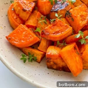 A speckled ceramic plate filled with perfectly roasted sweet potatoes, garnished with fresh green herbs. The sweet potatoes are golden, slightly caramelized, and bursting with savory-sweet flavor, ready to be served.