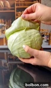 Two hands are peeling an outer leaf from a large, fresh green cabbage with a bakery background blurred in the distance.