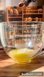 Protein Packed Pancake Bites 5 A thin stream of liquid is pouring from an espresso machine into a clear KitchenAid mixing bowl containing a yellow mixture, with shelves of bread in the background.