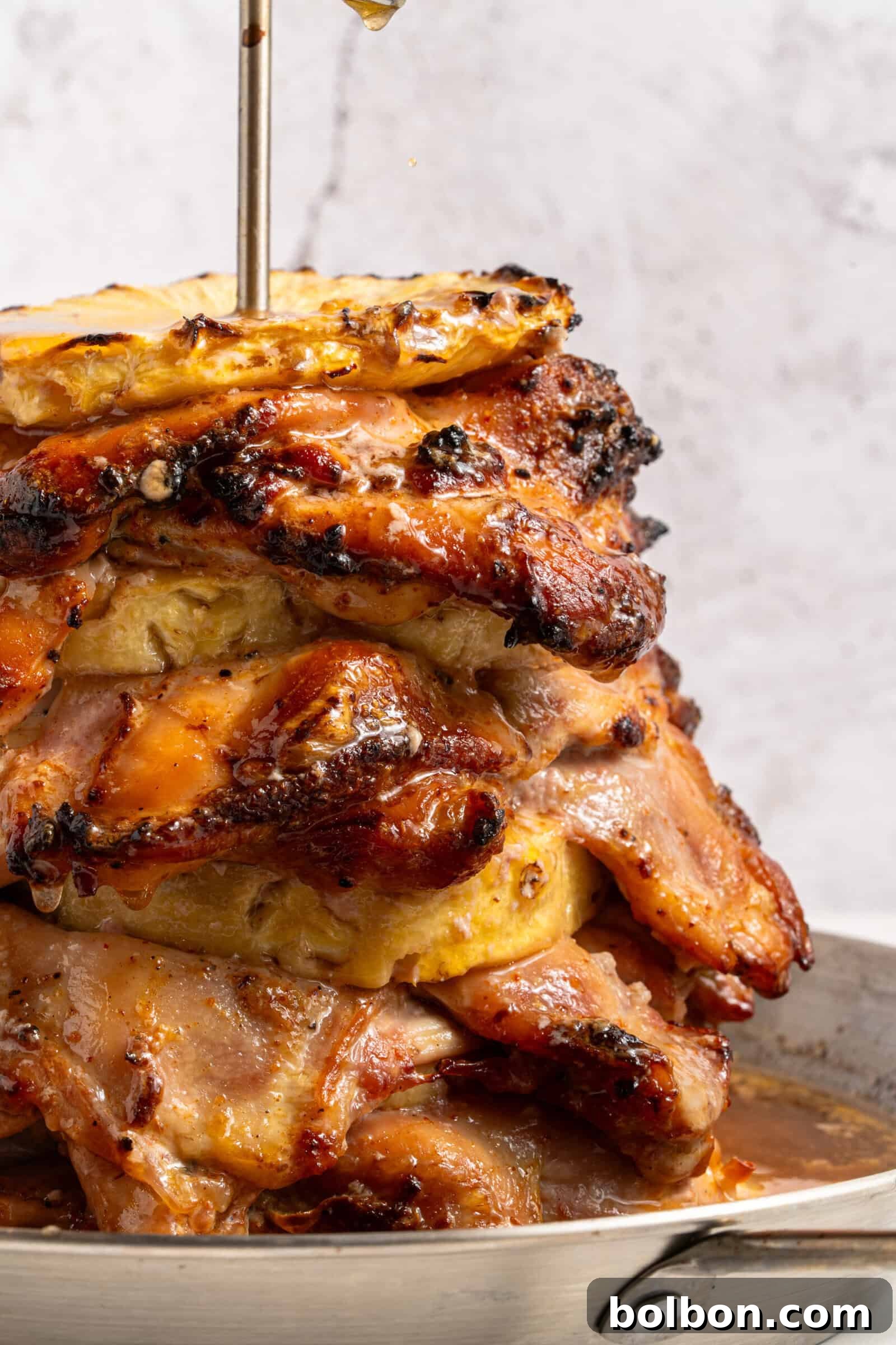 Aloha Chicken Gyro 2 A stunning vertical shot of a beautifully cooked pineapple chicken gyro, featuring golden-brown, spiced chicken thighs stacked on a vertical spit with caramelized pineapple rings. The meat is glistening with juices, ready to be sliced for serving.