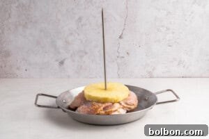 Aloha Chicken Gyro 7 A metal pan holds raw marinated chicken pieces stacked with a pineapple slice on top, all skewered vertically with a metal rod, against a light background.