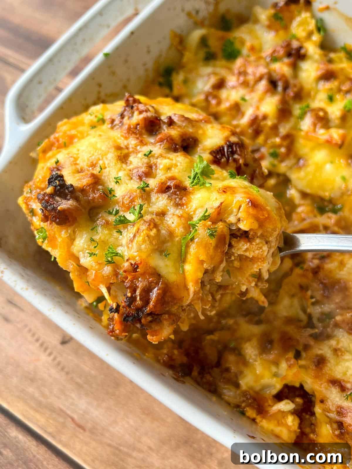 Layered Cabbage Comfort 2 A close-up of a cheesy, golden-brown Cabbage Lasagna being lifted from a baking dish with a spoon, topped with melted cheese and garnished with chopped parsley.