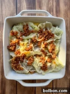 Layered Cabbage Comfort 13 A white baking dish filled with cabbage rolls topped with a chunky tomato and meat sauce, set on a wooden surface.