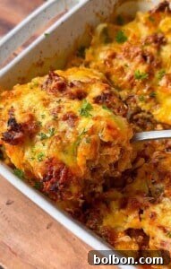 Layered Cabbage Comfort 14 A close-up of a casserole dish filled with cheesy baked casserole. A serving is being lifted out with a spoon, showing layers of melted cheese, ground meat, and herbs, garnished with fresh parsley.