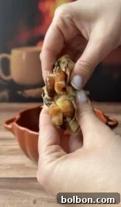 A close-up of hands squeezing roasted garlic cloves from the bulb over a brown bowl, with a blurred mug and warm background—perfect for flavoring Sweet Potato Stacks.