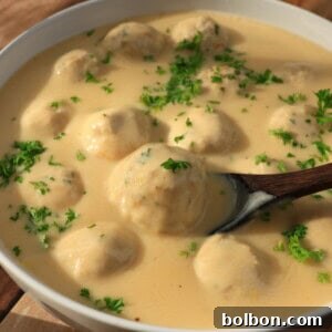 A bowl of creamy sauce with meatballs, garnished with chopped fresh parsley, sits on a wooden table. A wooden spoon is partially submerged in the sauce, ready to serve.