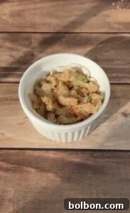 A white ramekin partially filled with a mixture of chopped shrimp, green herbs, and seasonings, sitting on a wooden surface, beautifully illuminated by direct sunlight, ready for the next layer.