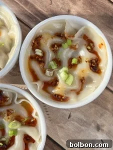A close-up shot of perfectly steamed Shrimp Dumpling Lasagna in a pristine white bowl, beautifully topped with a vibrant red drizzle of chili oil and garnished with a sprinkle of fresh green onions, all presented on a rustic wooden surface.