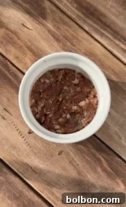 A white bowl filled with a mixture of minced meat and herbs sits on a wooden surface, lit by natural sunlight.