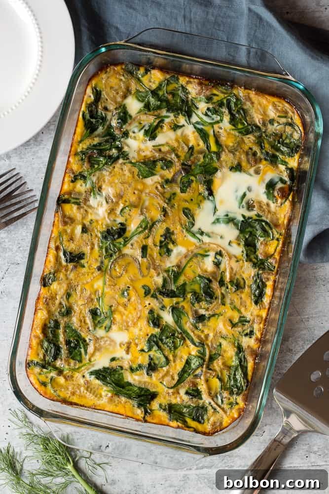 Close-up shot of the raw Make Ahead Breakfast Casserole ingredients layered in a glass baking dish, showing sausage, sautéed onions, fennel, and spinach beneath the poured egg mixture, ready for overnight refrigeration.