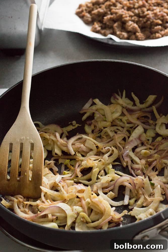 Cooked red onion and sliced fennel bulb sautéing in a pan until translucent and lightly browned, a key step for the breakfast casserole's flavor.