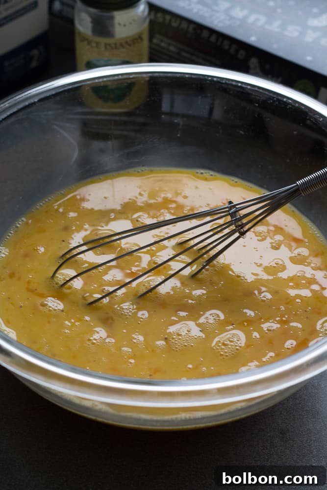 Close-up of the egg mixture in a glass bowl, whisked with milk, salt, and pepper, ready to be poured over the casserole ingredients.