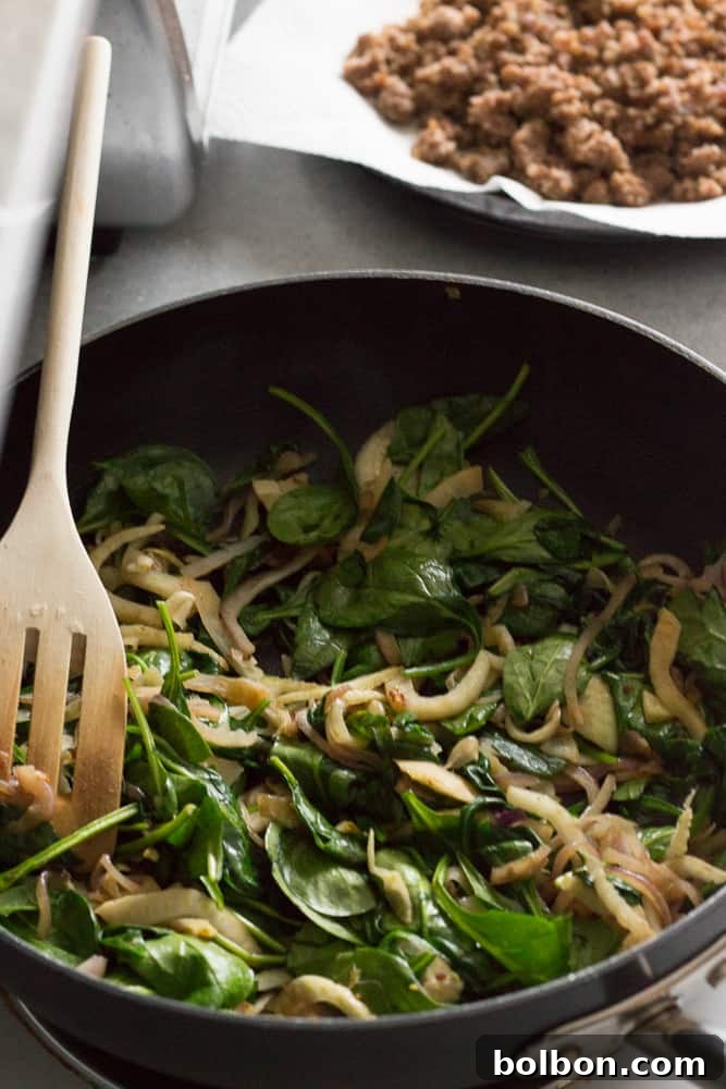 Fresh baby spinach wilting in a hot pan with sautéed onions and fennel, prepared for the make-ahead breakfast casserole.