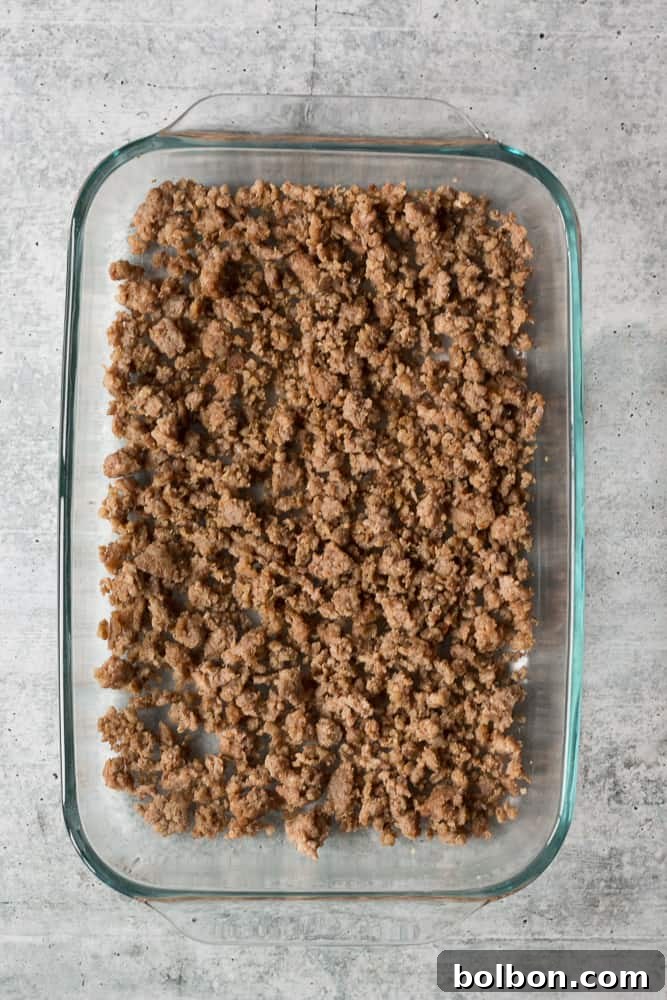 Cooked breakfast sausage spread in an even layer at the bottom of a greased 9x13 baking dish, ready for other casserole ingredients.