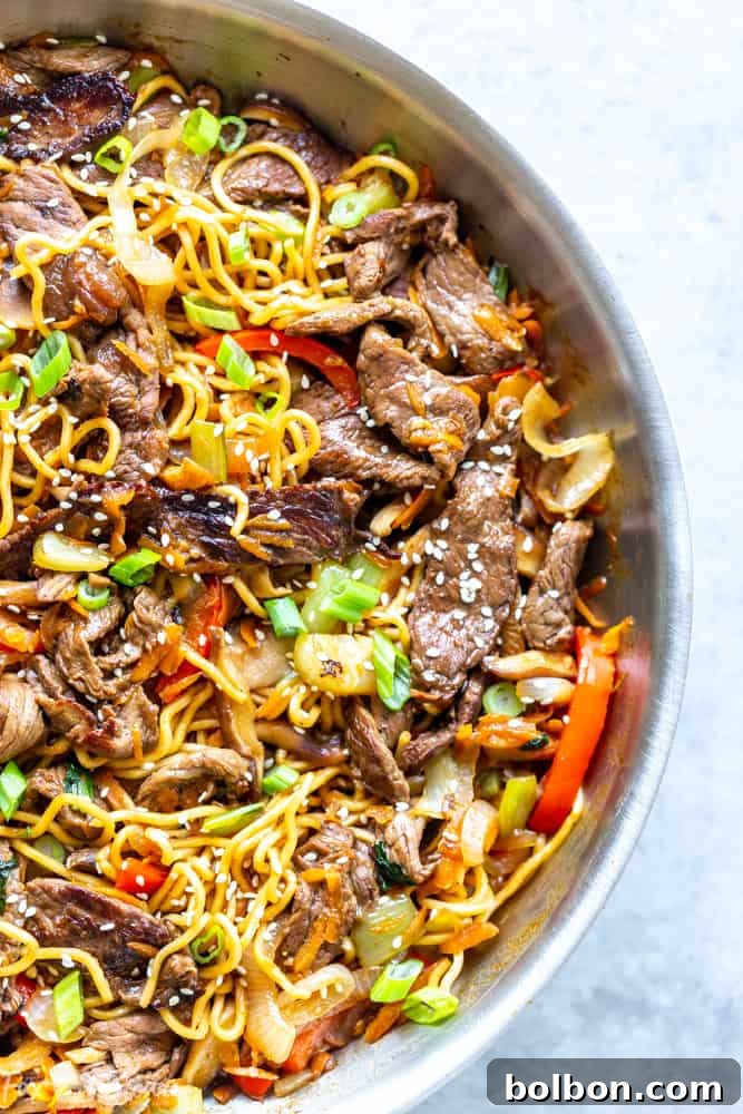 Hand holding chopsticks with a portion of homemade Beef Ramen Noodle Stir Fry, highlighting the delicious textures and fresh ingredients.