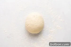 A ball of dough sits on a white surface lightly dusted with flour.