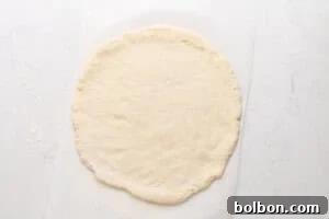 Pizza dough being rolled out on a floured surface with a rolling pin.