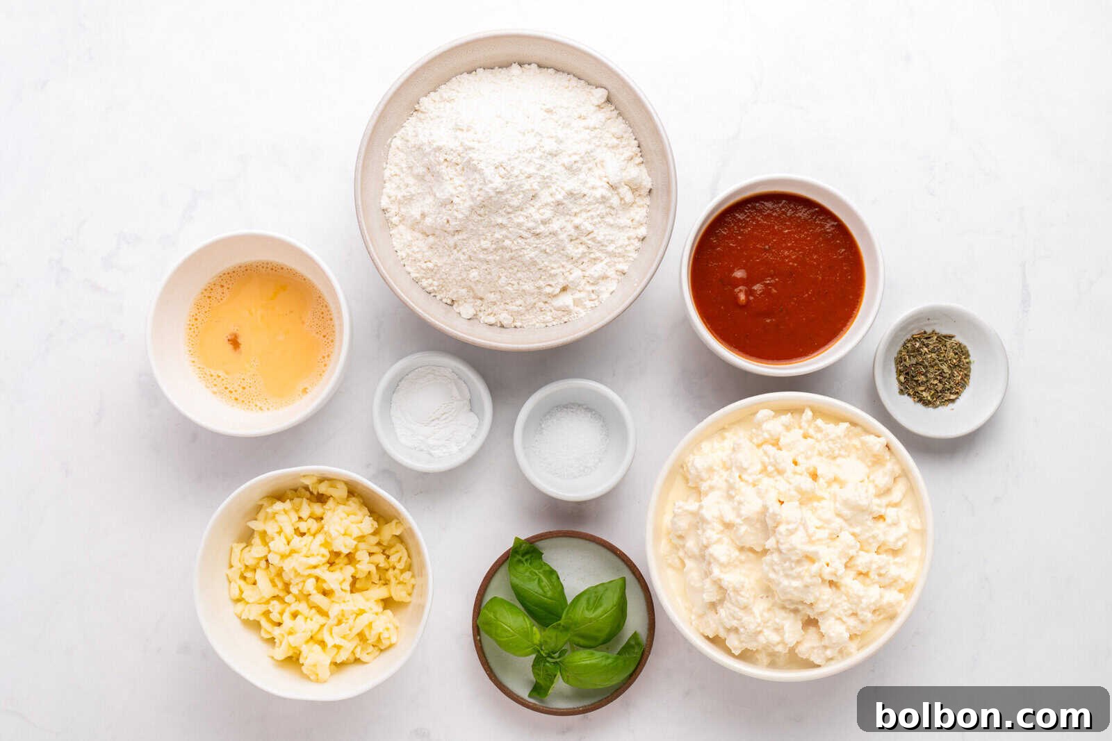 Various pizza ingredients in bowls on a white surface, including all-purpose flour, tomato sauce, shredded cheese, ricotta cheese, beaten egg, baking powder, salt, dried herbs, and fresh basil leaves.