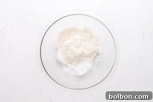 High-Protein Cottage Cheese Flatbreads 5 A clear glass bowl containing a mixture of dry baking ingredients, including flour and possibly sugar or baking powder, on a white marble surface.