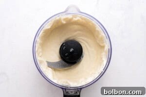 High-Protein Cottage Cheese Flatbreads 6 A food processor filled with smooth, creamy mixture is viewed from above on a white surface. The metal blade is visible in the center, surrounded by the blended mixture.
