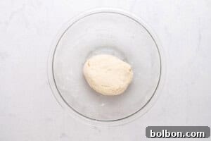 High-Protein Cottage Cheese Flatbreads 7 A clear glass bowl containing a ball of smooth, pale dough sits on a white marble surface.