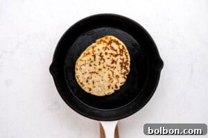 High-Protein Cottage Cheese Flatbreads 11 A single piece of flatbread is cooking in a black cast iron skillet with a white handle, set on a white marble surface.