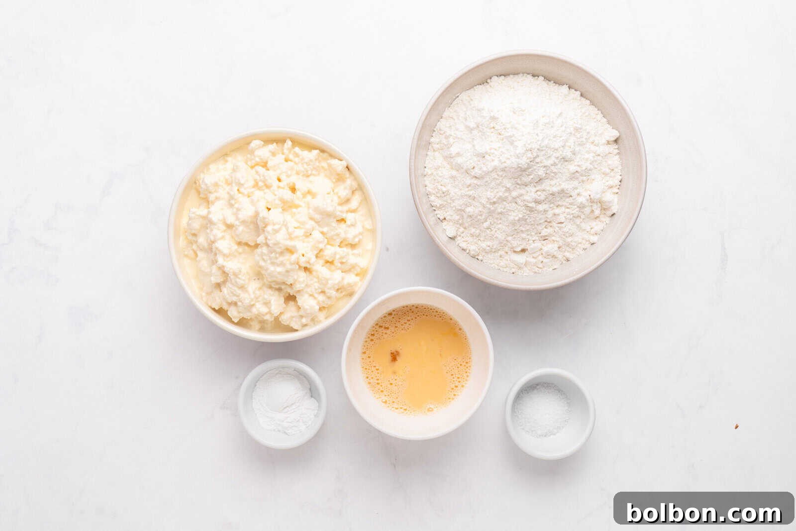 High-Protein Cottage Cheese Flatbreads 3 Five bowls on a white surface: one with cottage cheese, one with flour, one with beaten egg, one with baking powder, and one with salt.