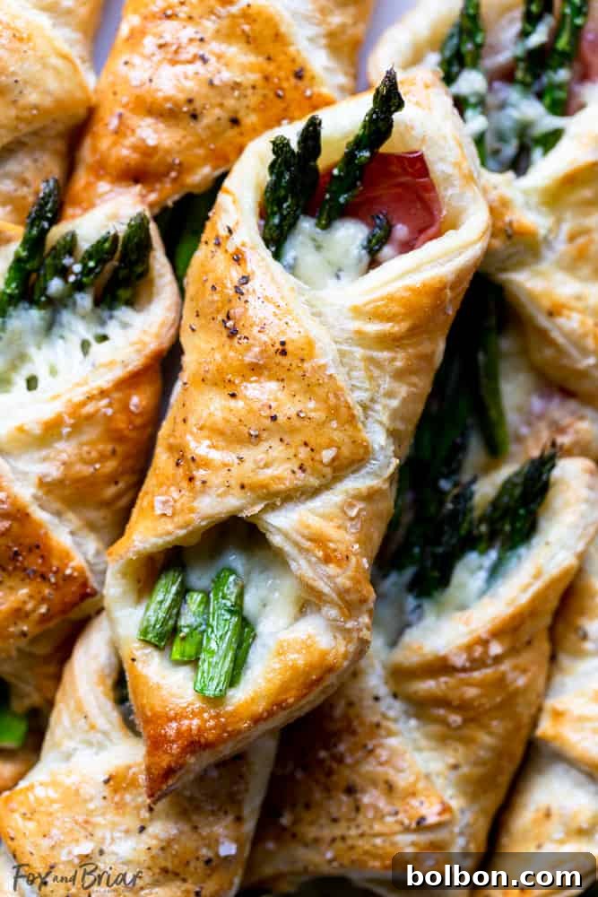 A baking sheet filled with golden, puffed Prosciutto Asparagus Puff Pastry Bundles fresh out of the oven.