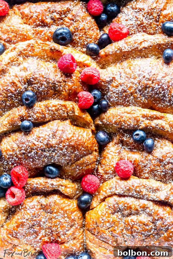 Overnight Croissant French Toast Strata 2 Close up of Croissant French Toast in pan with berries scattered on top, showcasing golden crust and tender interior