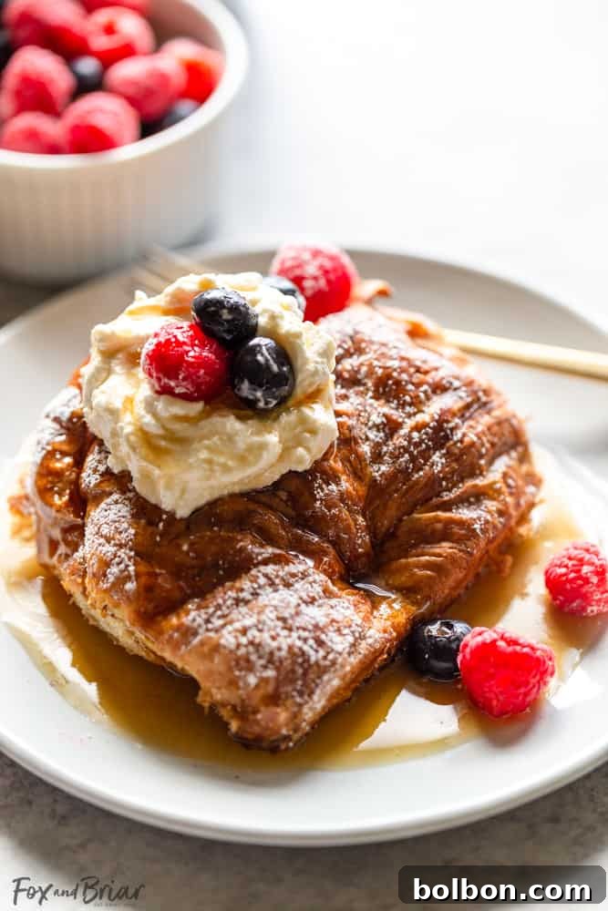 Overnight Croissant French Toast Strata 5 Overnight Croissant French Toast Bake in a baking dish with a spoon, highlighting its fluffy texture