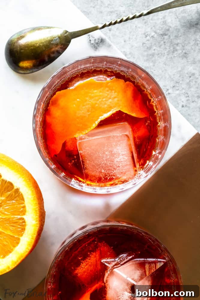 Closeup overhead of Negroni cocktail with ice and an orange peel garnish, resting on a table.