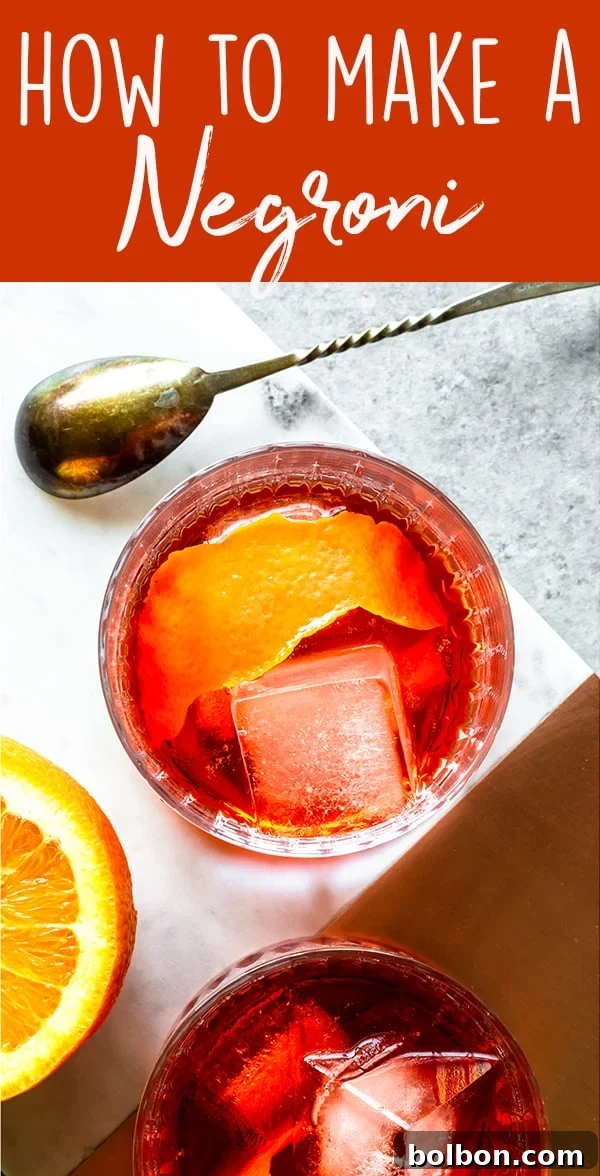 Two hands stirring a Negroni in a rocks glass with a bar spoon, demonstrating preparation.