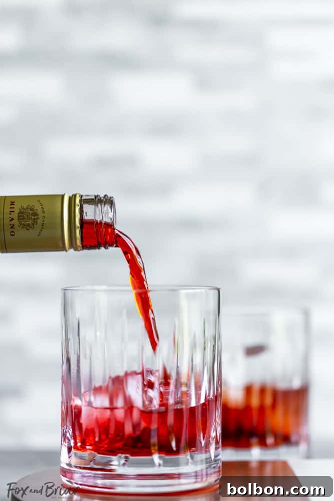 A bartender pouring vibrant red Campari into a cocktail glass filled with ice.