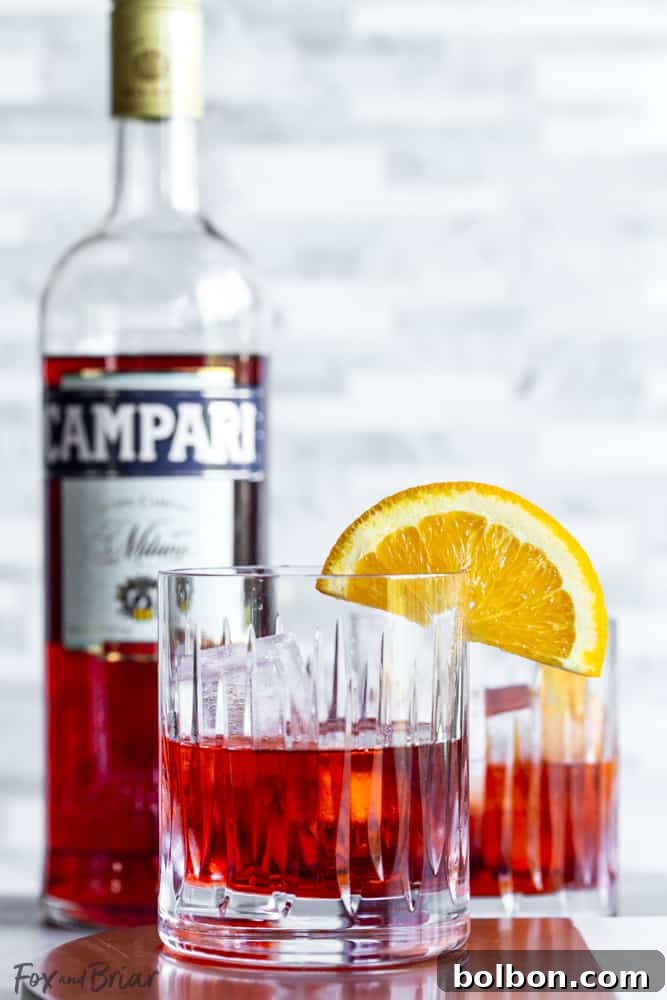 A perfectly prepared Negroni cocktail with an orange peel garnish, next to a bottle of Campari.