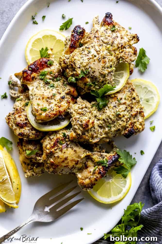 Beautifully roasted Greek chicken thighs served on a white plate with fresh lemon wedges and parsley, highlighting their golden-brown finish.