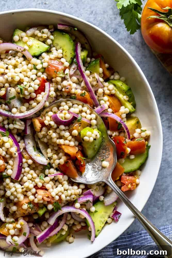 Easy Pearl Couscous Salad: A quick and healthy vegan side dish or light lunch, ideal for cookouts and summer entertaining. Serving Israeli couscous salad from a white bowl with a large spoon, showcasing its pearl-like texture and colorful vegetables
