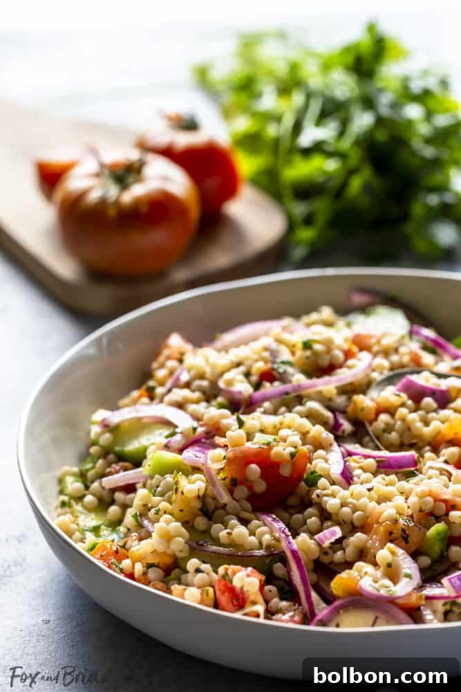 Healthy Couscous Salad Recipe: A vibrant, easy-to-make cold pasta salad with pearl couscous and fresh vegetables, perfect for any occasion. A beautifully presented serving of vegan couscous salad in a pristine white bowl, garnished with fresh herbs