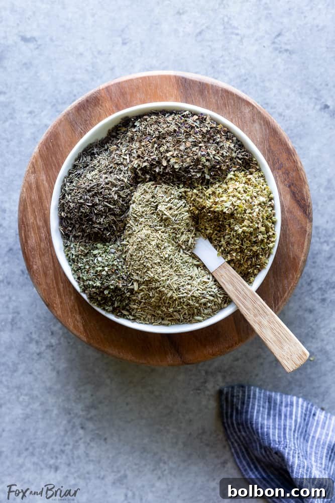 Various dried herbs, including whole rosemary and fennel, arranged on a rustic wooden board before grinding.