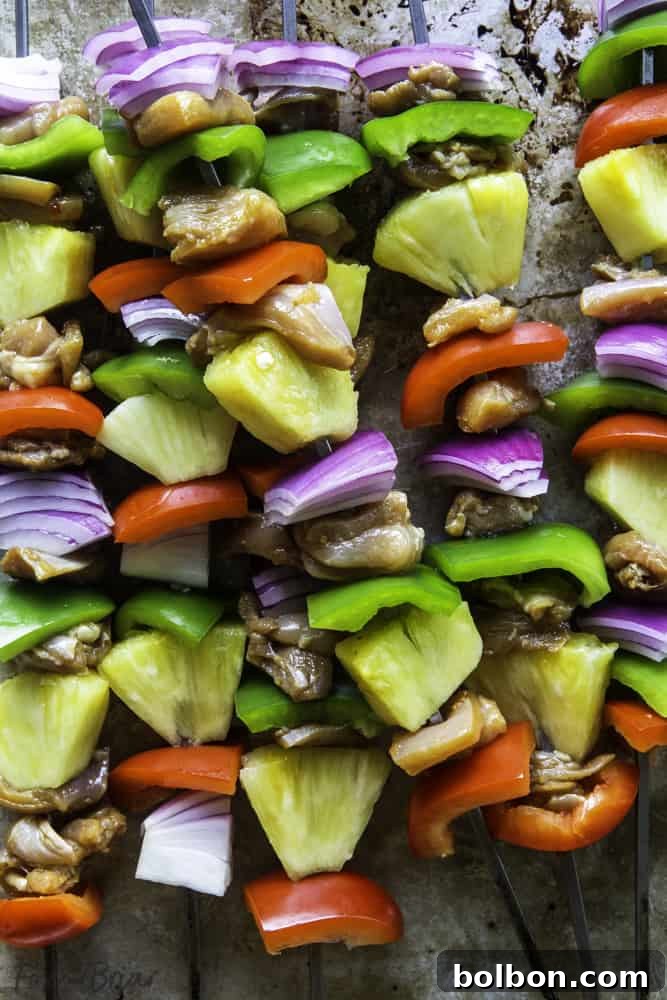 Skewers of raw Hawaiian Chicken Kabobs, neatly arranged with cubed chicken, vibrant bell peppers, red onion, and fresh pineapple, ready for grilling.