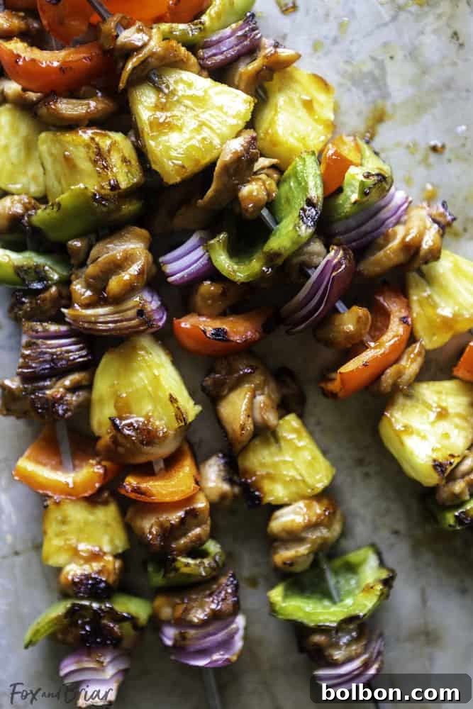 A hand carefully threading marinated chicken, vibrant bell peppers, and sweet pineapple chunks onto a sturdy metal skewer in an alternating pattern.