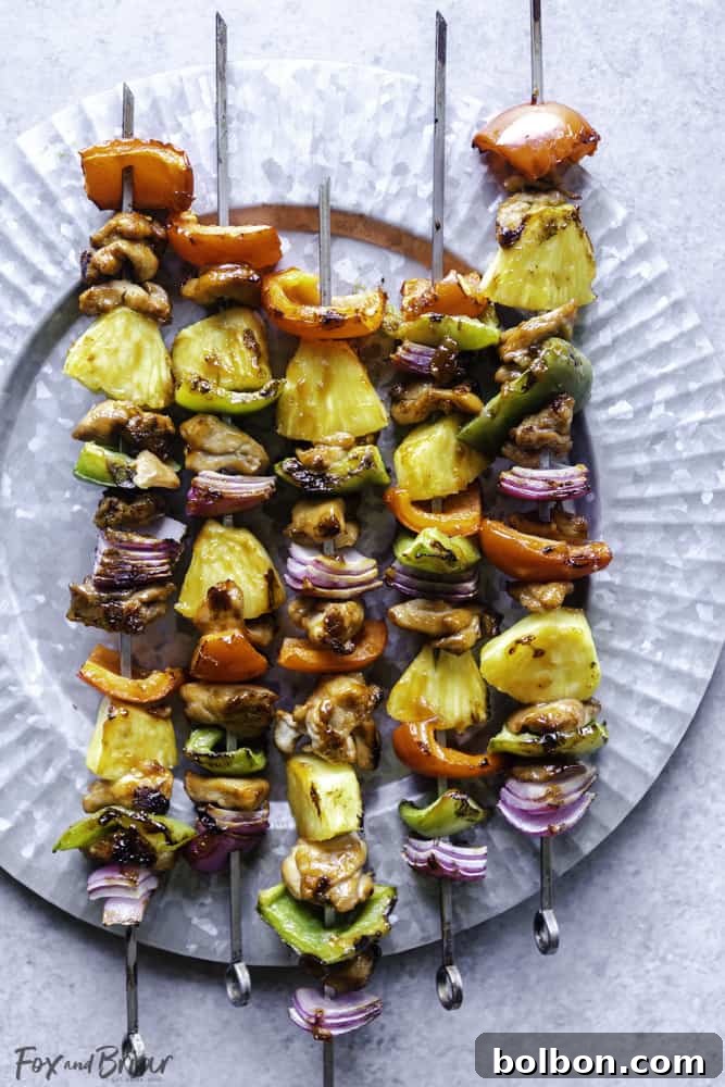 A final close-up shot of the perfectly grilled Hawaiian Chicken Kabobs artfully arranged on a rustic wooden platter, garnished with fresh cilantro.