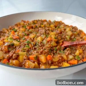 A close-up of a bowl filled with a chunky stew resembling Moussaka with Potatoes, featuring ground meat, diced potatoes, carrots, and green herbs, with a wooden spoon resting inside. The dish appears hearty and freshly prepared.