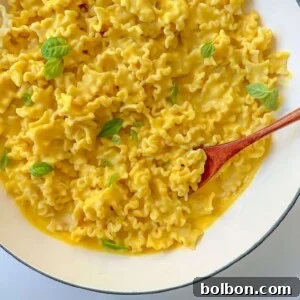 A white bowl filled with ruffled Creamy Butternut Squash Pasta in a silky yellow sauce, garnished with fresh basil leaves, and a wooden spoon resting in the dish.