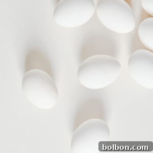 Several white eggs are scattered across a light, neutral background, creating a minimalistic and clean appearance—perfect for illustrating techniques like how to cut deviled eggs. Soft shadows add depth to the composition.
