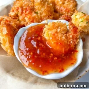Golden, crispy coconut shrimp—made from our signature Coconut Shrimp Recipe—served in a basket with a small white dish of sweet chili dipping sauce, all nestled on parchment paper.