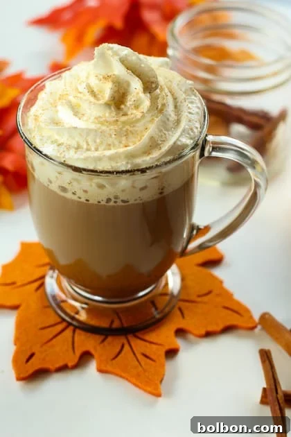 Hand holding a mug of coffee with Autumn Spice Syrup, steaming gently, on a backdrop of blurred fall leaves