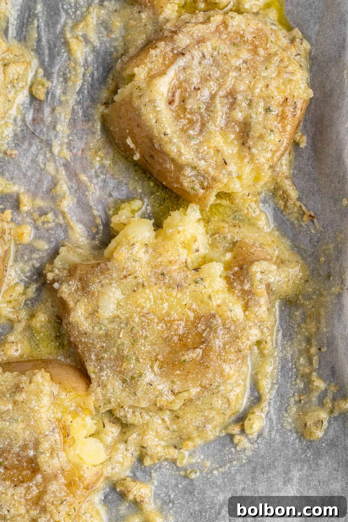 Close-up of entree topped with melted cheese on a parchment-lined baking sheet. The golden cheese is slightly crusted, covering the mashed pieces, and the surface is dotted with specks of seasoning.