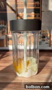 Protein-Packed Dutch Pancake 5 Milk is being poured into a glass blender cup containing egg yolks and egg whites, perfect for making a High Protein Dutch Baby, with a sunny kitchen and pastries visible in the blurred background.